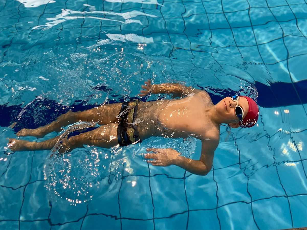 Criança praticando flutuação de costas na piscina