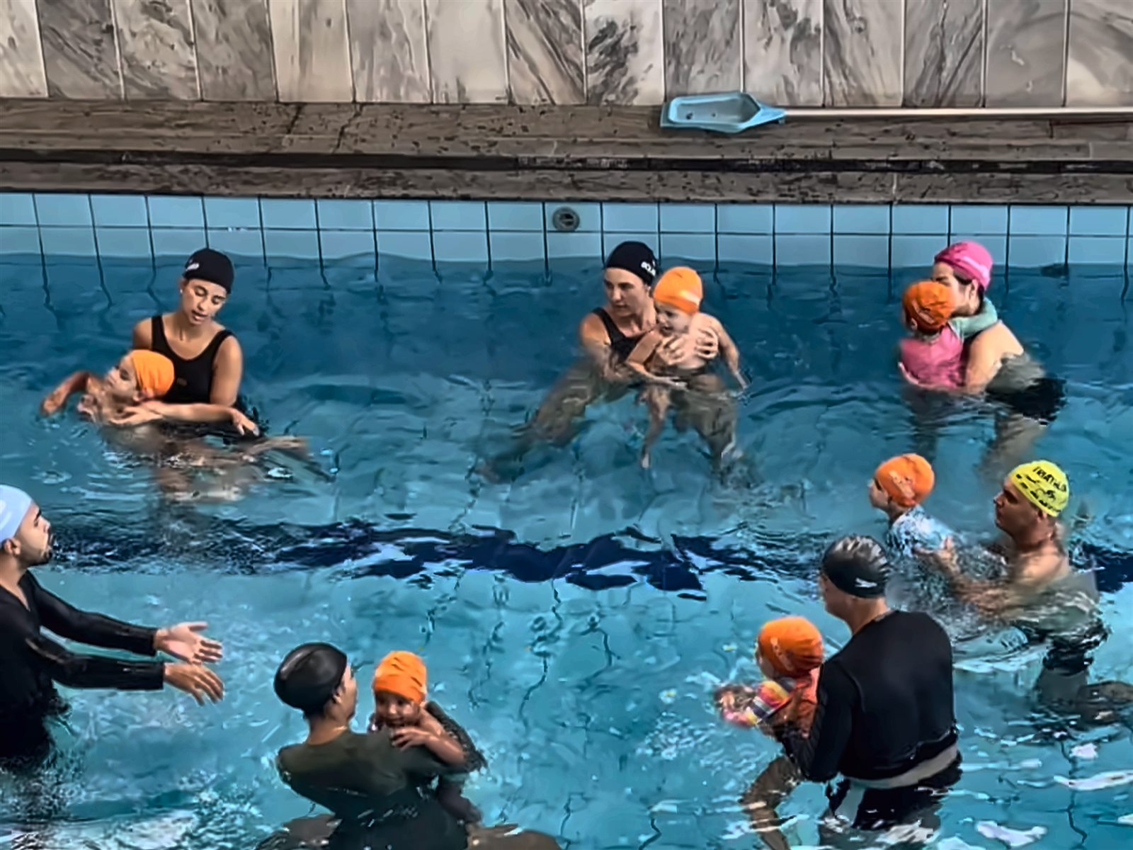 Turma de natação para bebês com familiares e professores na piscina